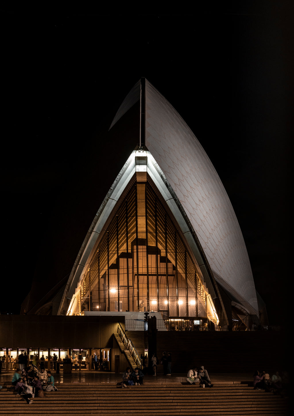 The Sydney Opera House lit up at night with people enjoying the public stairs