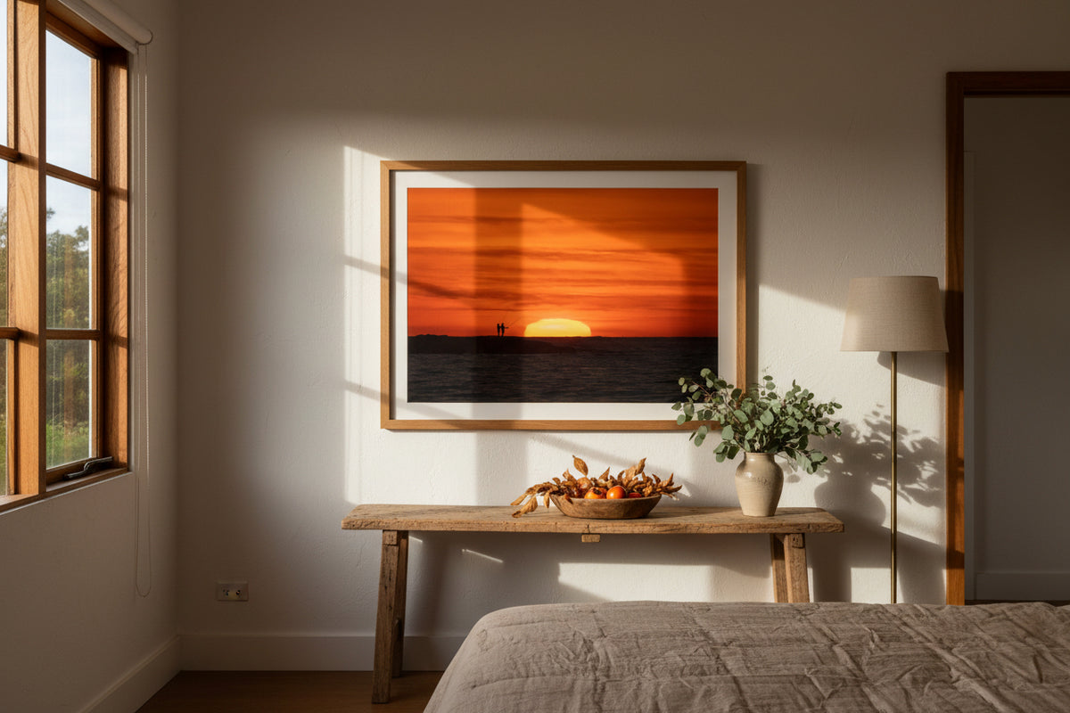 Two people standing on Ben Buckler at sunrise with an orange sky and silhouette of the sun.