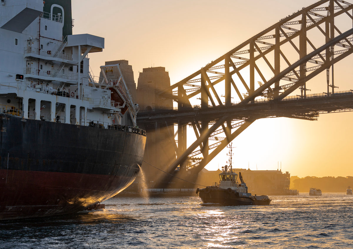A giant fuel tanker is escorted out of Sydney Harbour by a tug boat, just as the autumn sun sets over the Sydney Harbour Bridge