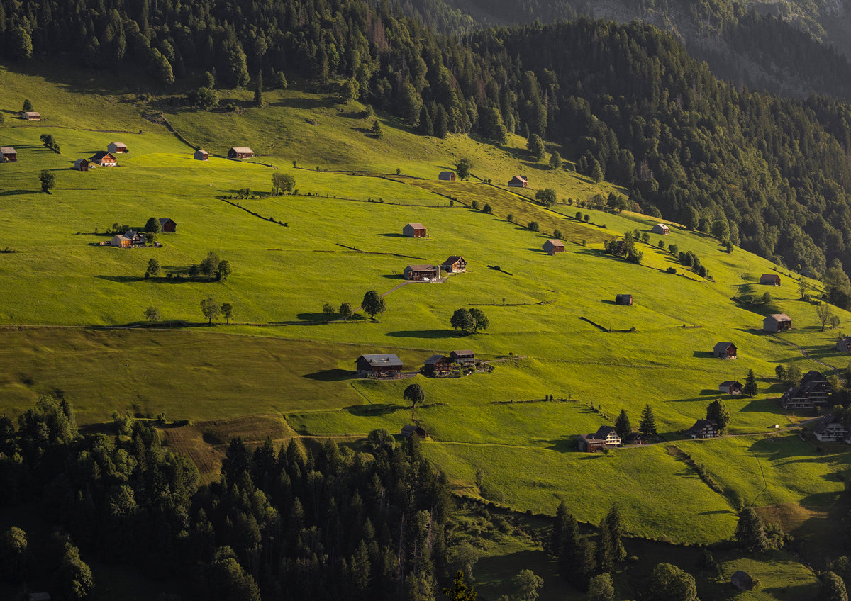 Green valley with scattered houses and trees, surrounded by forested hills.