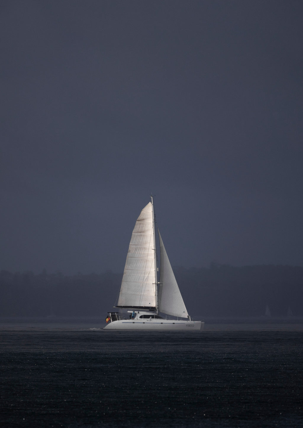 A sailboat cutting through the rain over Sydney Harbour, as lit up by the sun cutting through the clouds