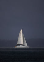 A sailboat cutting through the rain over Sydney Harbour, as lit up by the sun cutting through the clouds