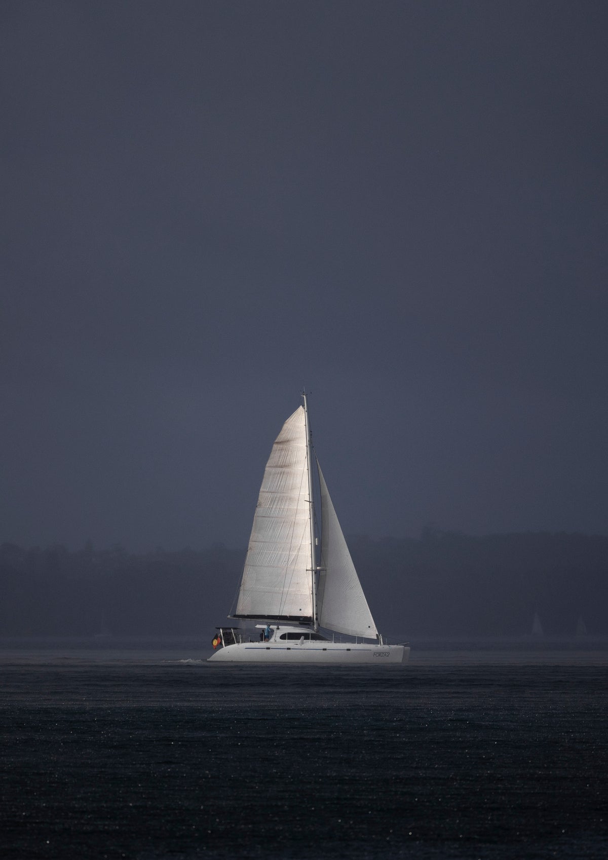 A sailboat cutting through the rain over Sydney Harbour, as lit up by the sun cutting through the clouds