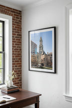 Tall clock tower in an urban setting with modern buildings.