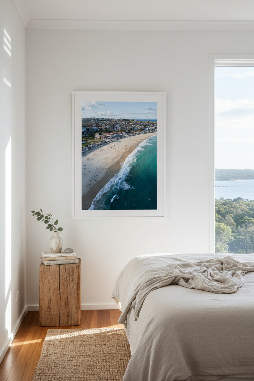 Aerial view of a Bondi Beach with waves crashing onto the shore and the Pavillion lit up by the sun.